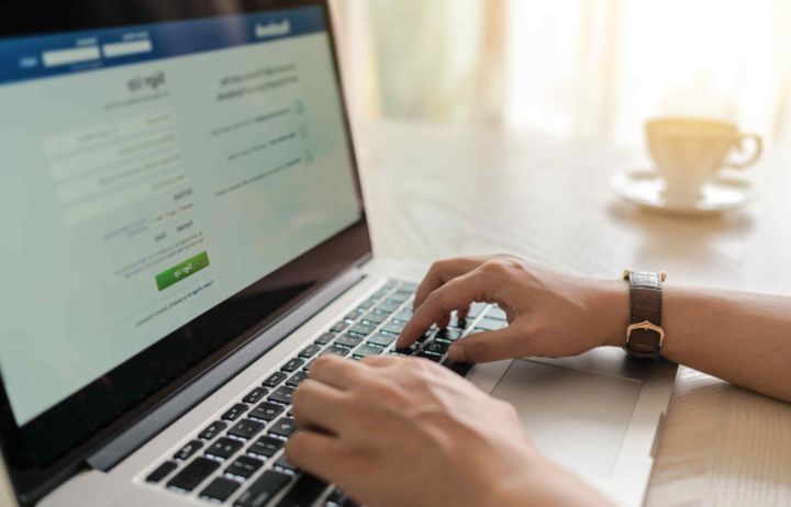 Man typing on a laptop displaying Facebook