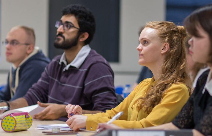 Students sat around a table listening to a maths lecture