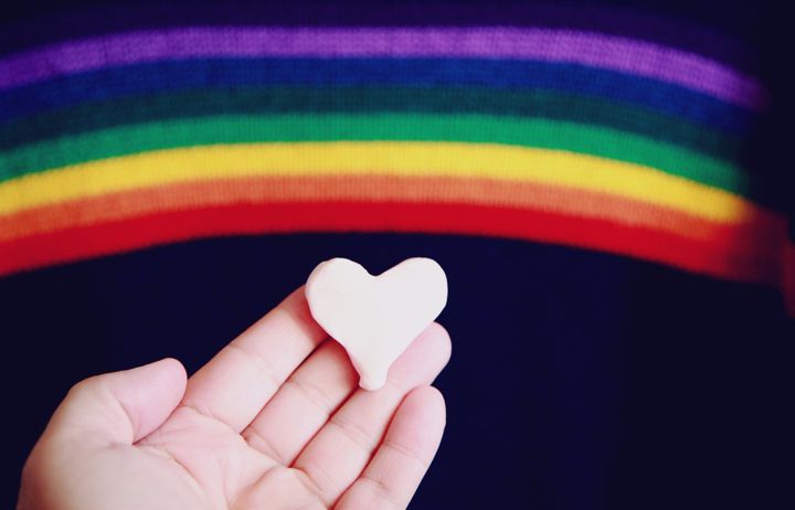 hand holding heart with rainbow background