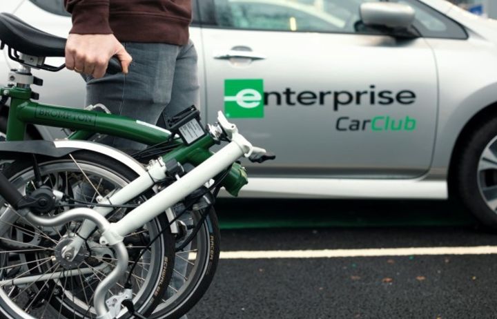 Person carrying a folding bike with a car in the background