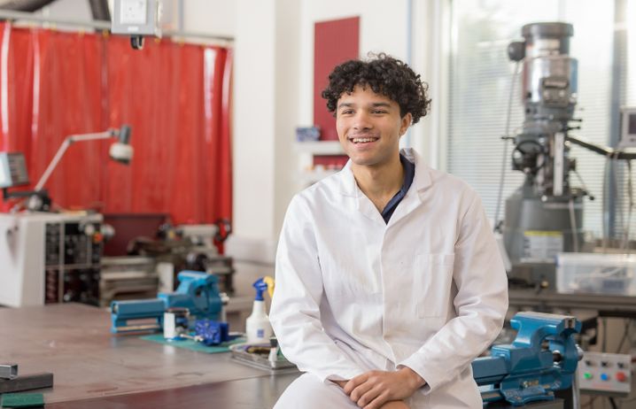 Undergraduate student in engineering lab sitting on workspace with clamps and equipment behind 