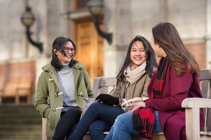 Three students talking and laughing on a bench