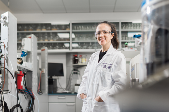 portrait of a female student in a lab, wearing protection glasses and a white overall