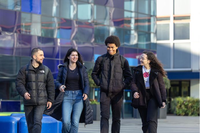 Four students laughing and walking together across Dalby Court.