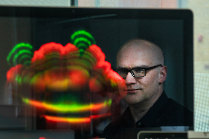 Professor Robert Endres looks to camera, surrounded by laptops with diagrams of patterms