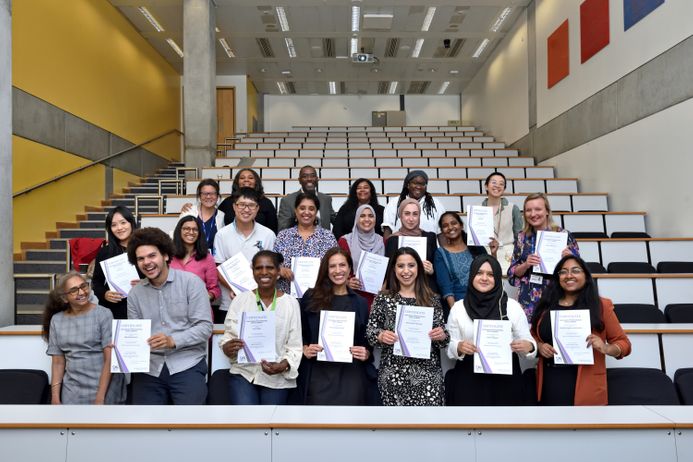 Group of staff from ethnic minority backgrounds standing in rows smiling and holding up certificates