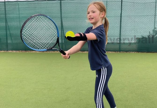 A young tennis player wearing one of Koalaa's soft prosthetics prepares to serve