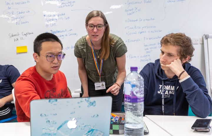 Three people looking at a laptop during a lesson