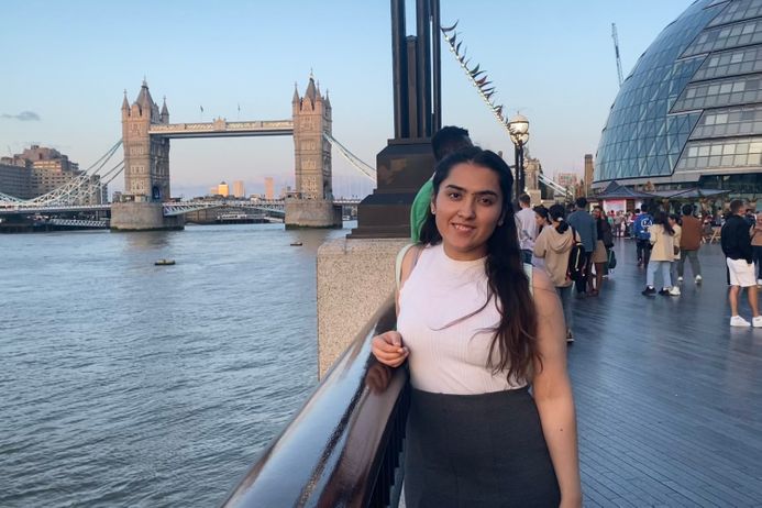 A female student standing along the Thames with Tower Bridge in the background.
