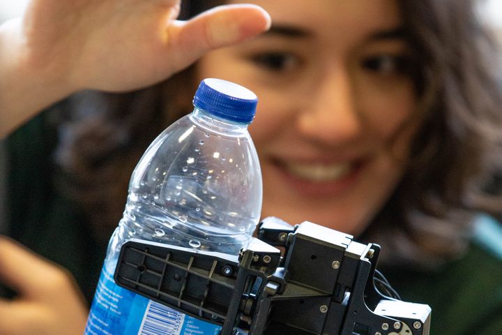 A student passes a plastic water bottle to a robotic gripping hand