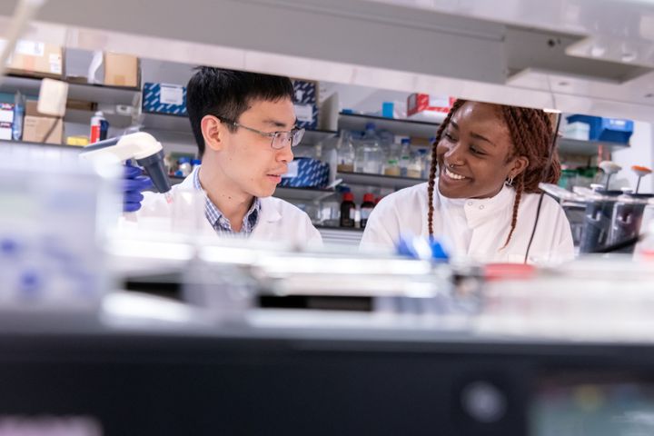 Two researchers smile at each other in white lab coats in the lab