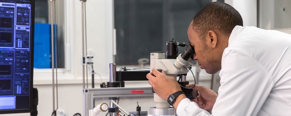 Dr Michael Madekurozwa looks into a microscope in a laboratory