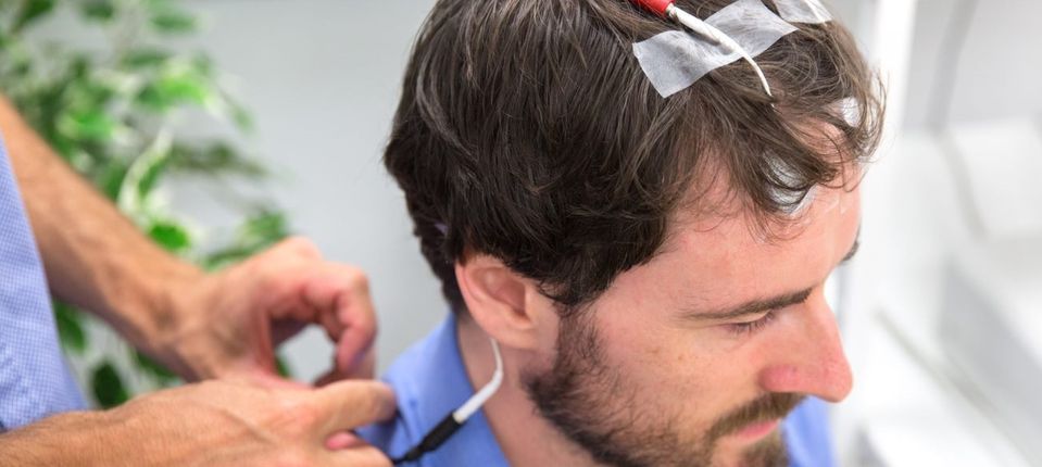 Hands adjusting a wire attached to electrodes on a man's forehead