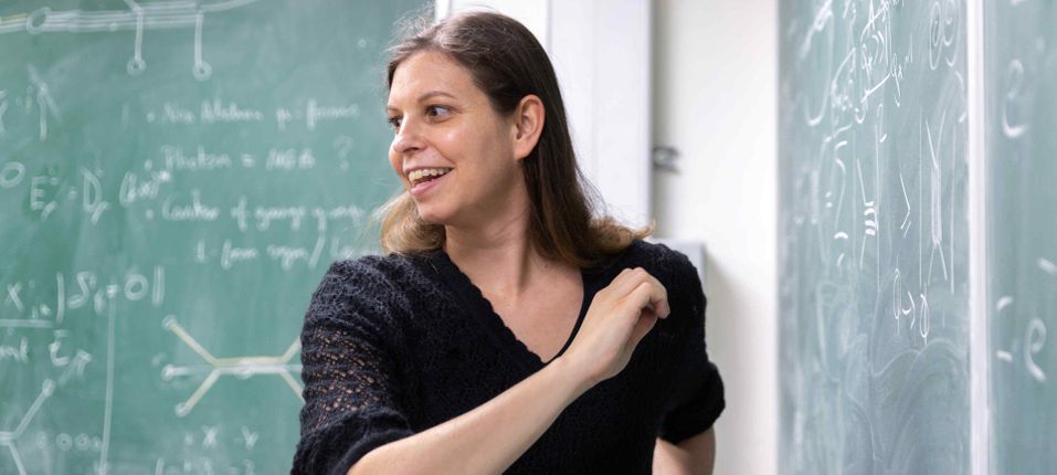 Professor Claudia De Rham writing equations at a board