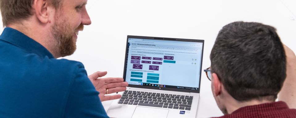 Two men in front of laptop showing CfAE self-study dashboard