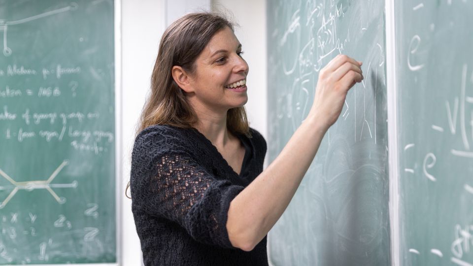 Claudia de Rham writing on a chalk board in one of the Physics lecture rooms