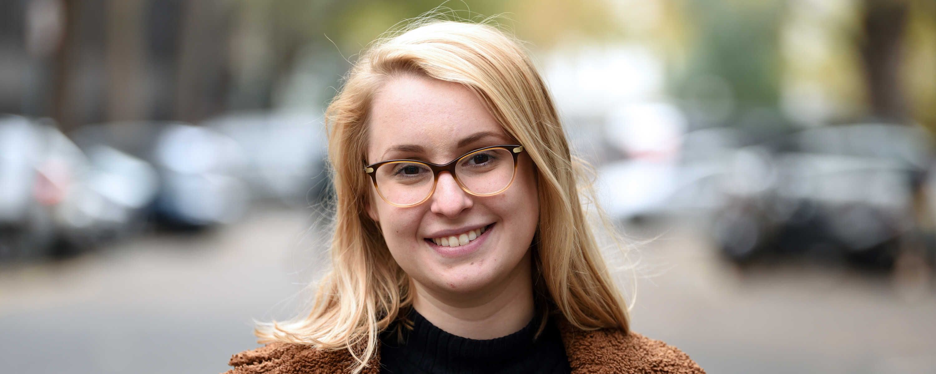 A portrait of Hannah Kay, one of the DeepMind scholars, smiling in the sunshine against a blurred background