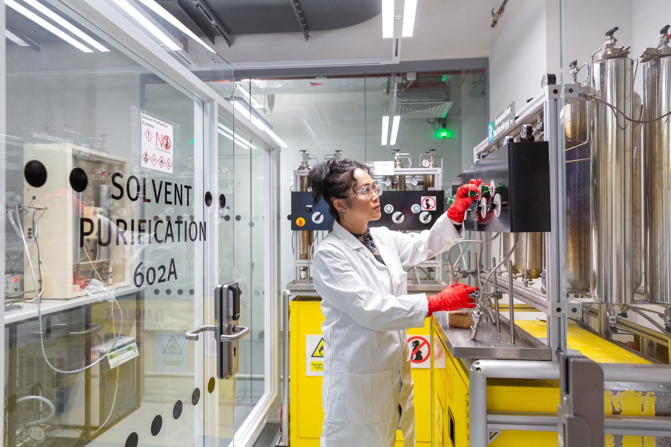 A technician wearing a lab coat, safety glasses and protective gloves adjusts dials on equipment in the Molecular Sciences Research Hub.