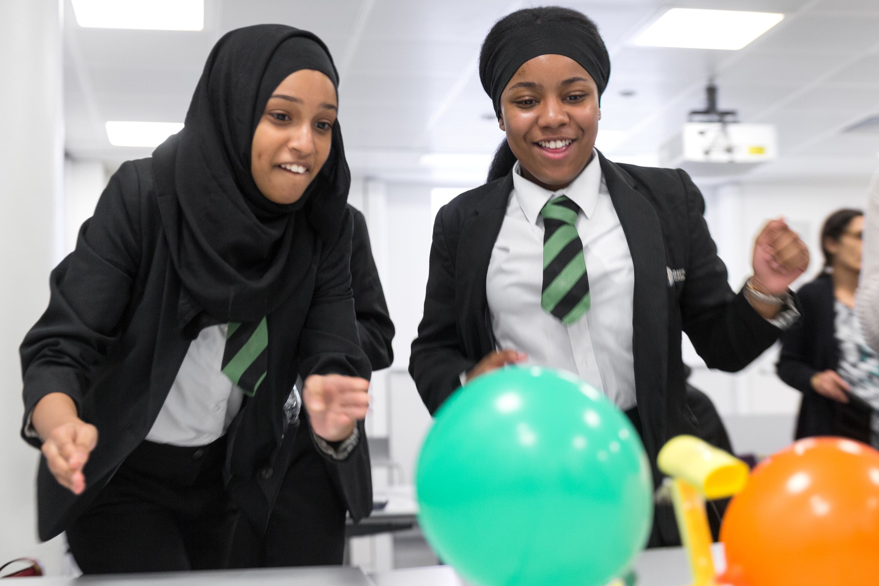 Two schoolgirls laughing as they carry out an experiment with balloons
