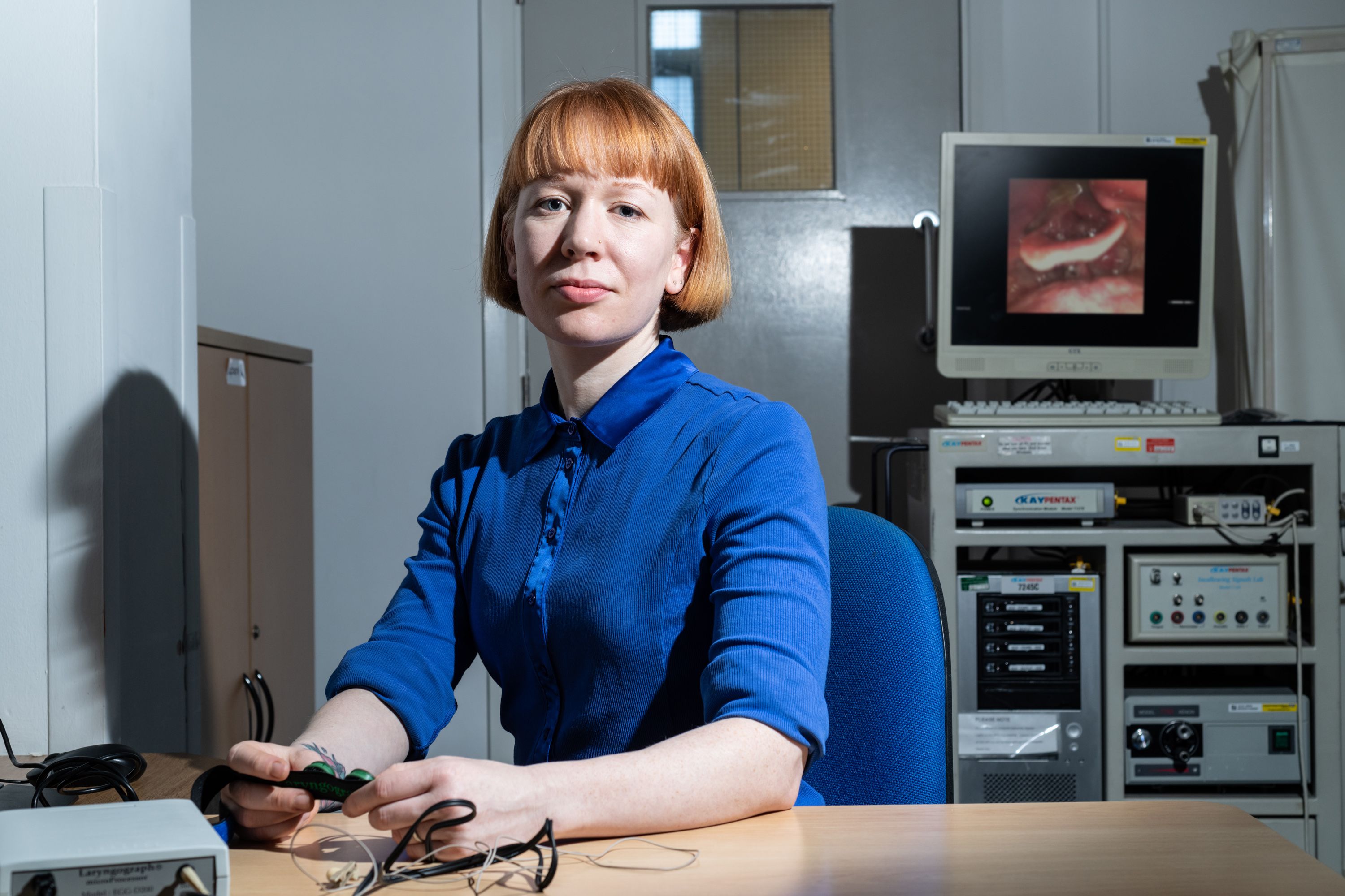 A portrait photograph of Gemma Clunie, sitting at a desk next to electronic equipment