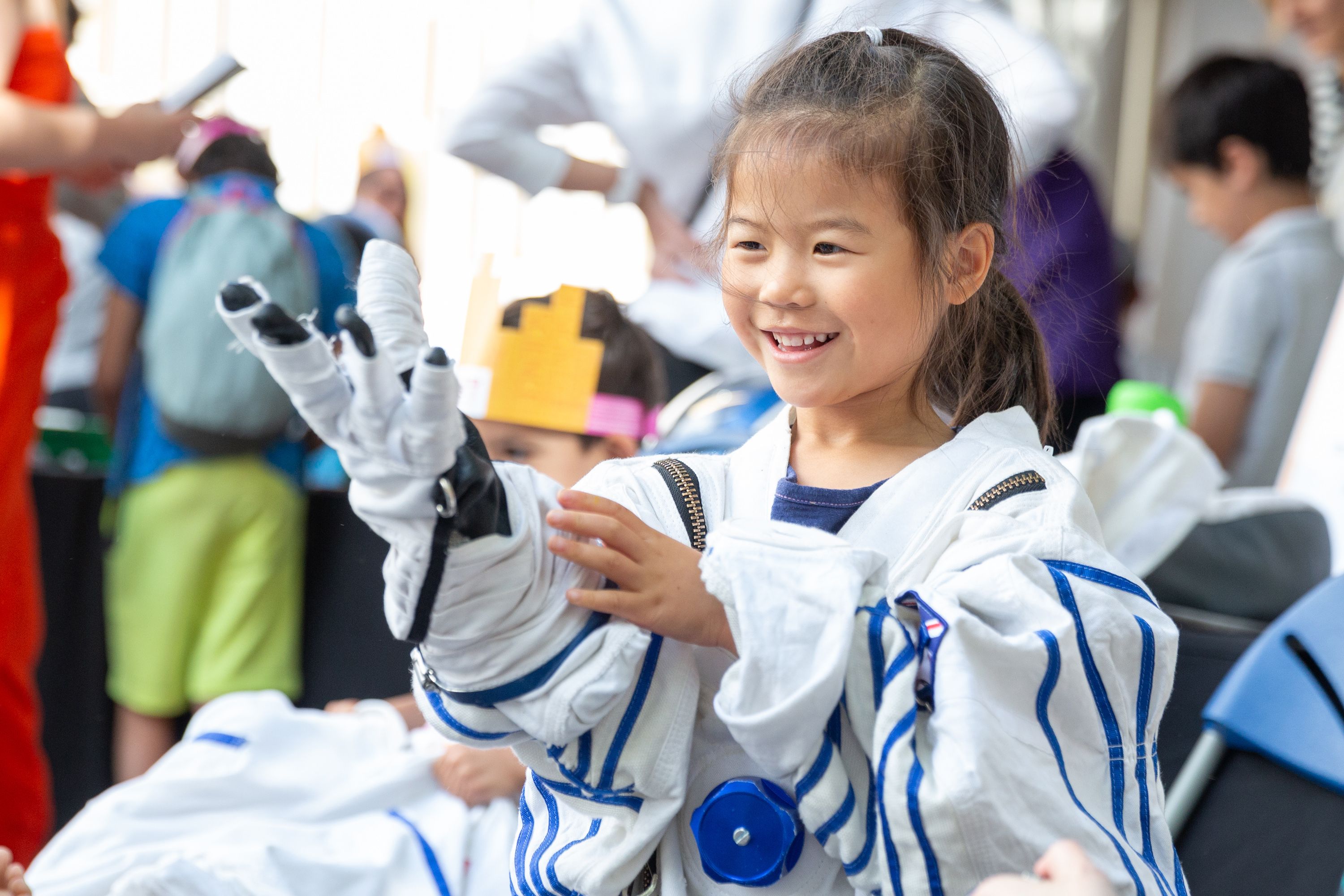 A young girl smiling as she tries on a space suit