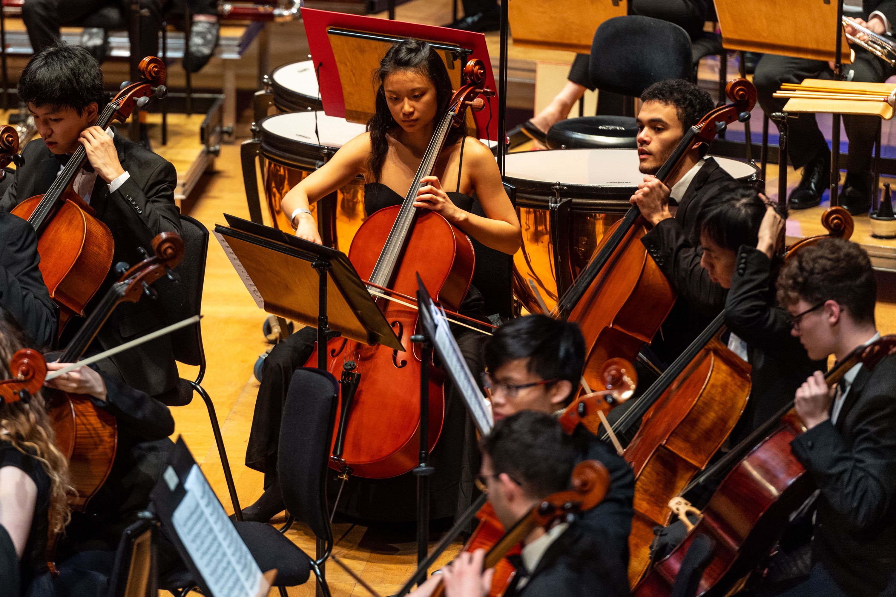 A shot of student cellists in formal attire playing in an orchestra