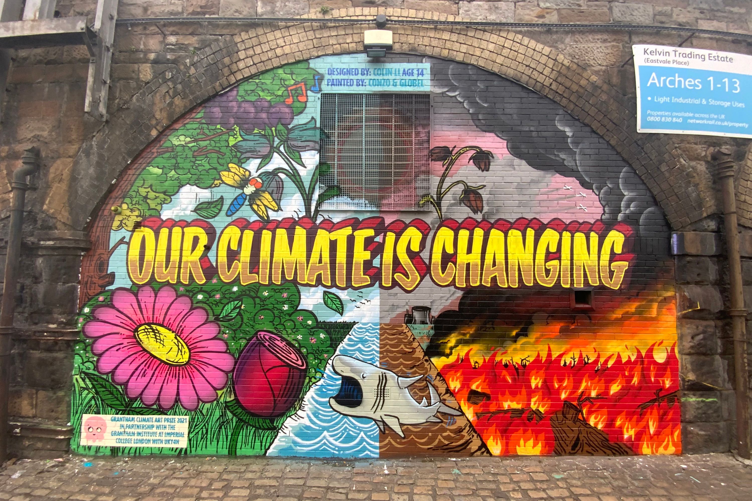A mural on a bricked up railway arch, divided in half with colourful nature on one side and a blasted apocalyptic wasteland on the other, and the words Our Climate is Changing