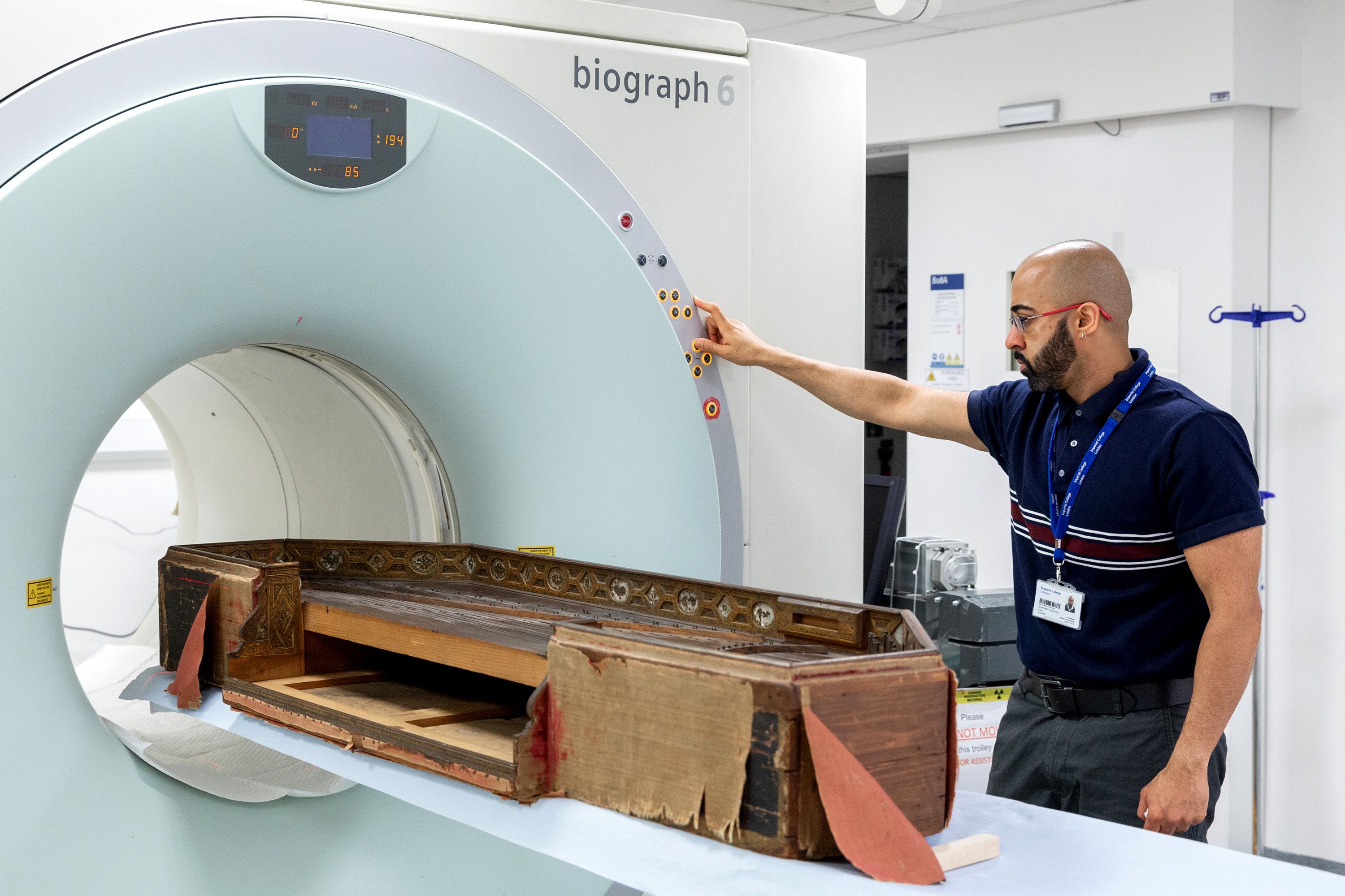 A technician stands over a 16th century harpsichord as it slides into the large white ring of a CT scanner