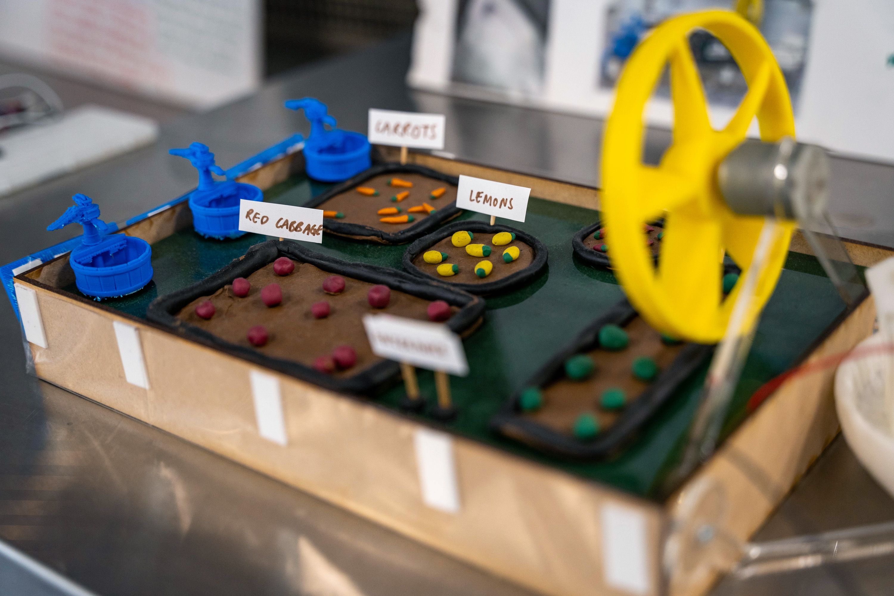 A close-up of a model of trays of fruit and vegetables, with a fan connected to a motor next to them