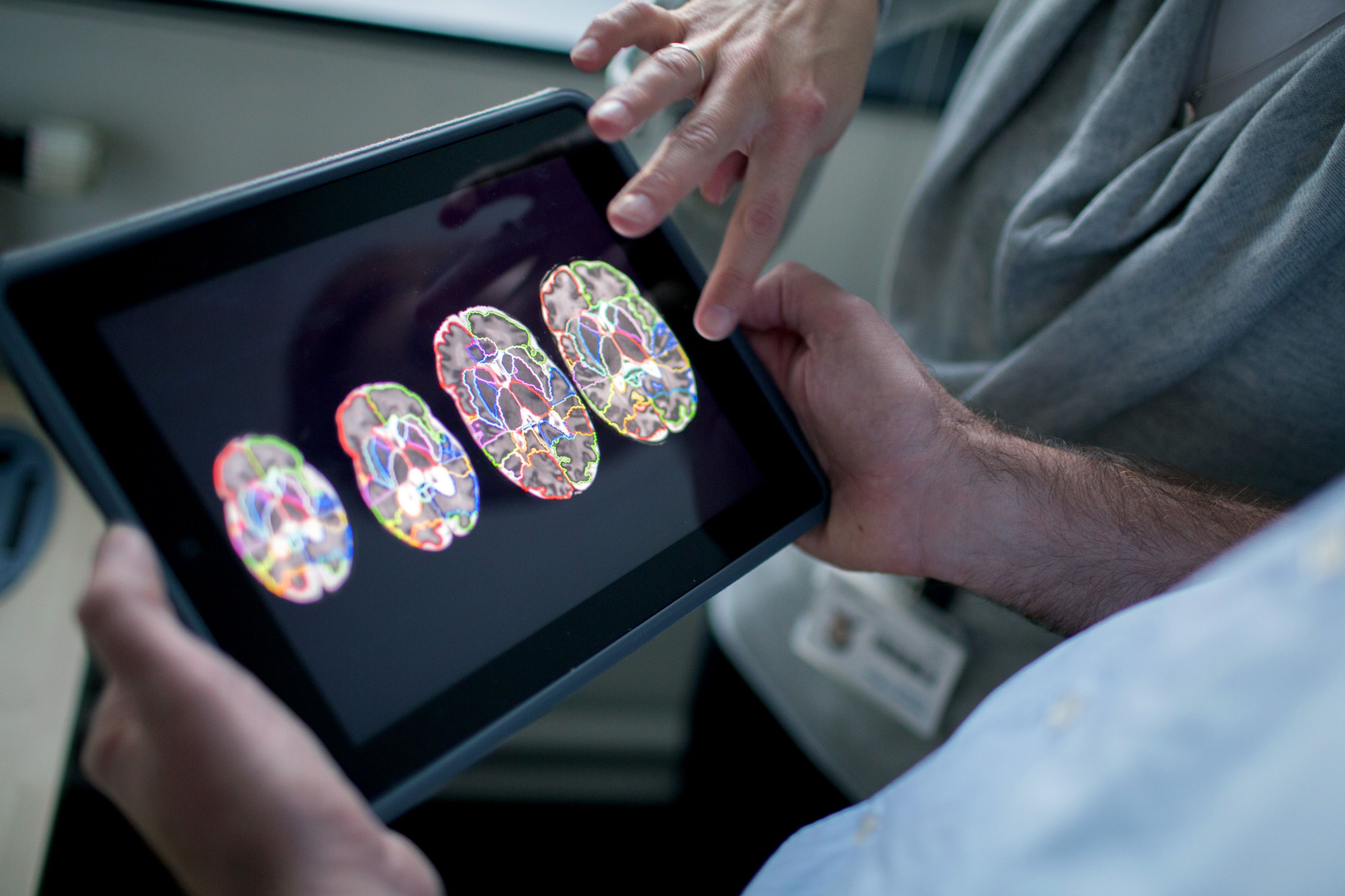 The hands of two people examining colourful brain scans on a tablet