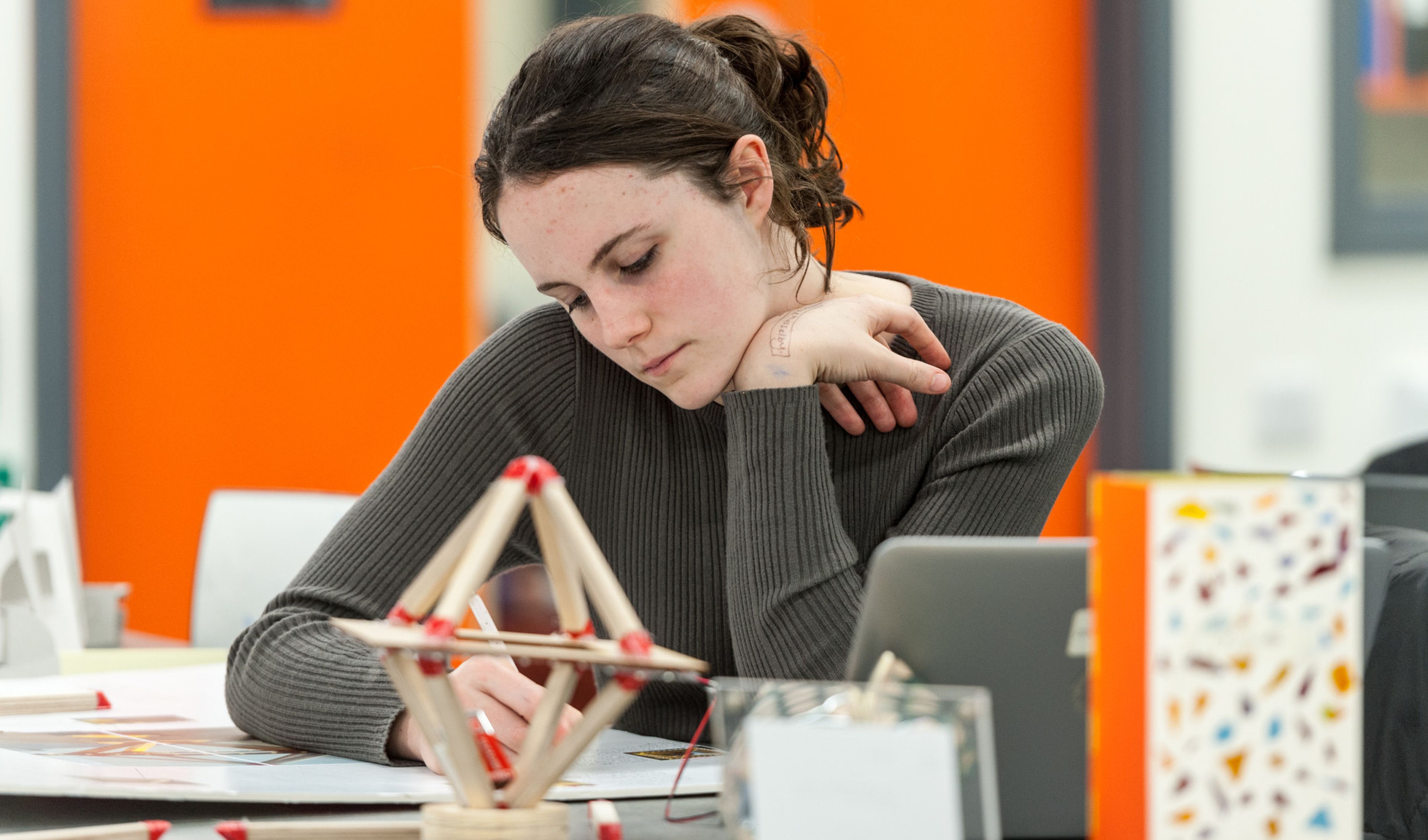 A secondary school student works on her project with her prototype in front of her.
