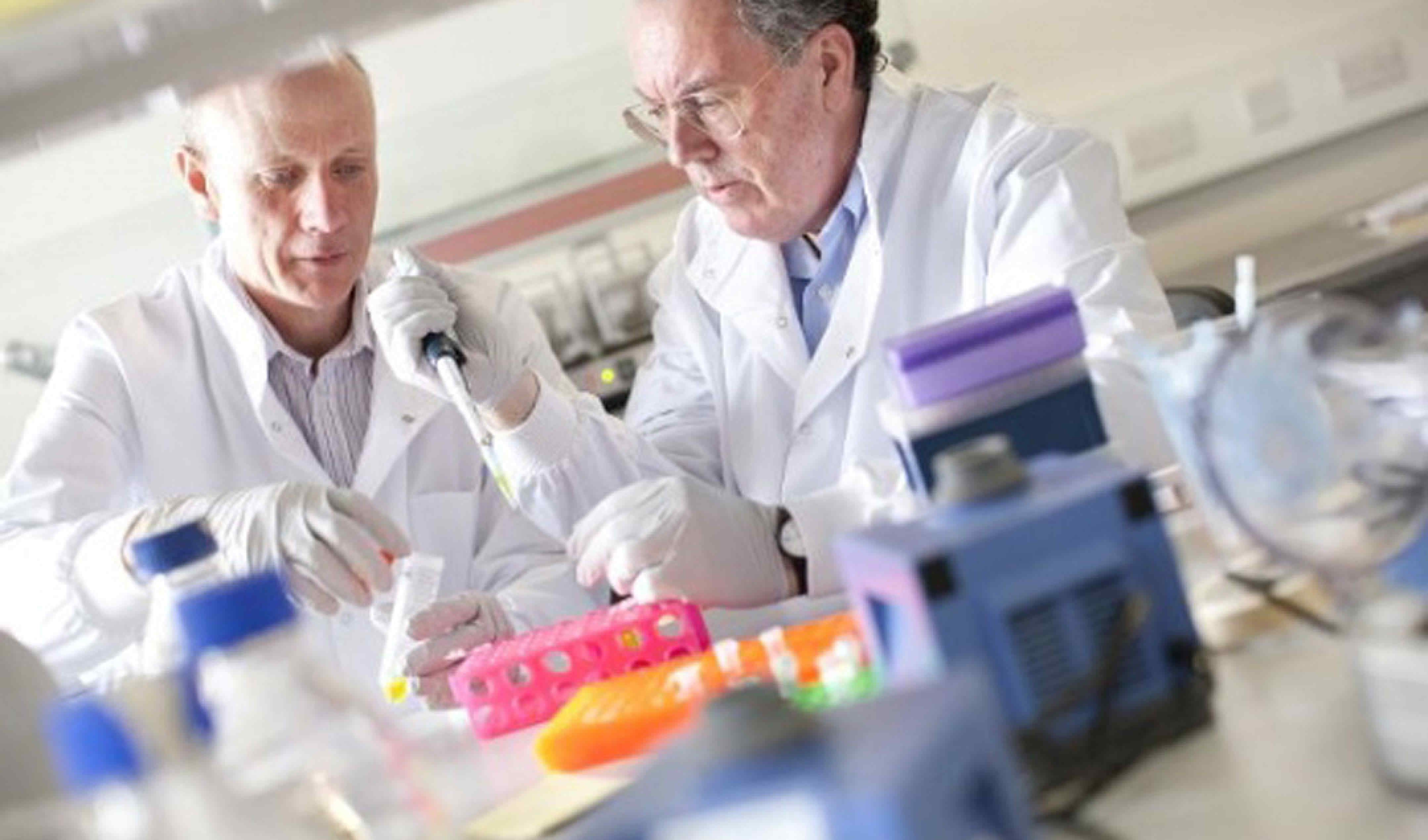 Professors Freemont and Kitney aring lab coats pipetting liquid into test tubes