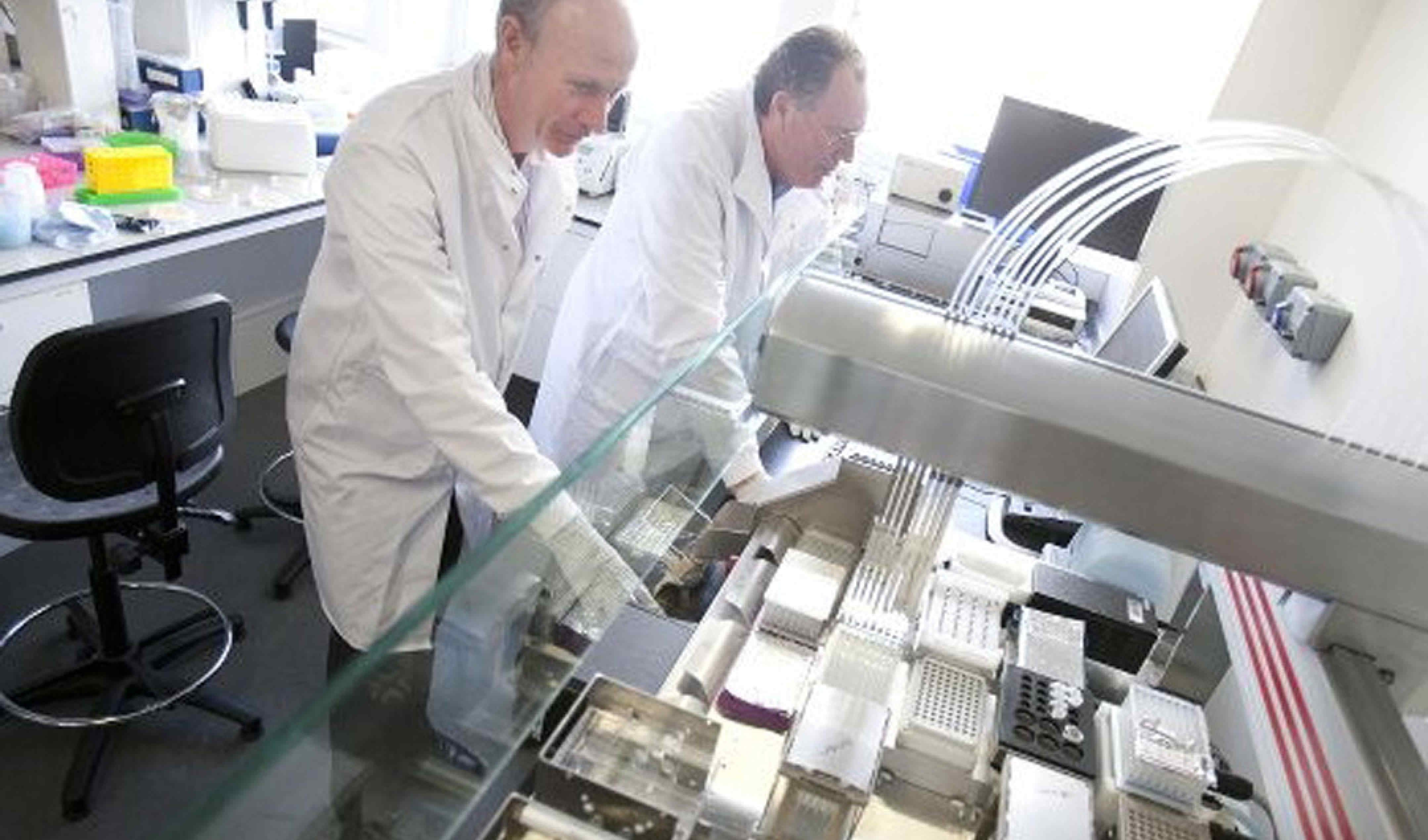 Professors Freemong and Kitney wearing lab coats working at a lab bench behind a screen