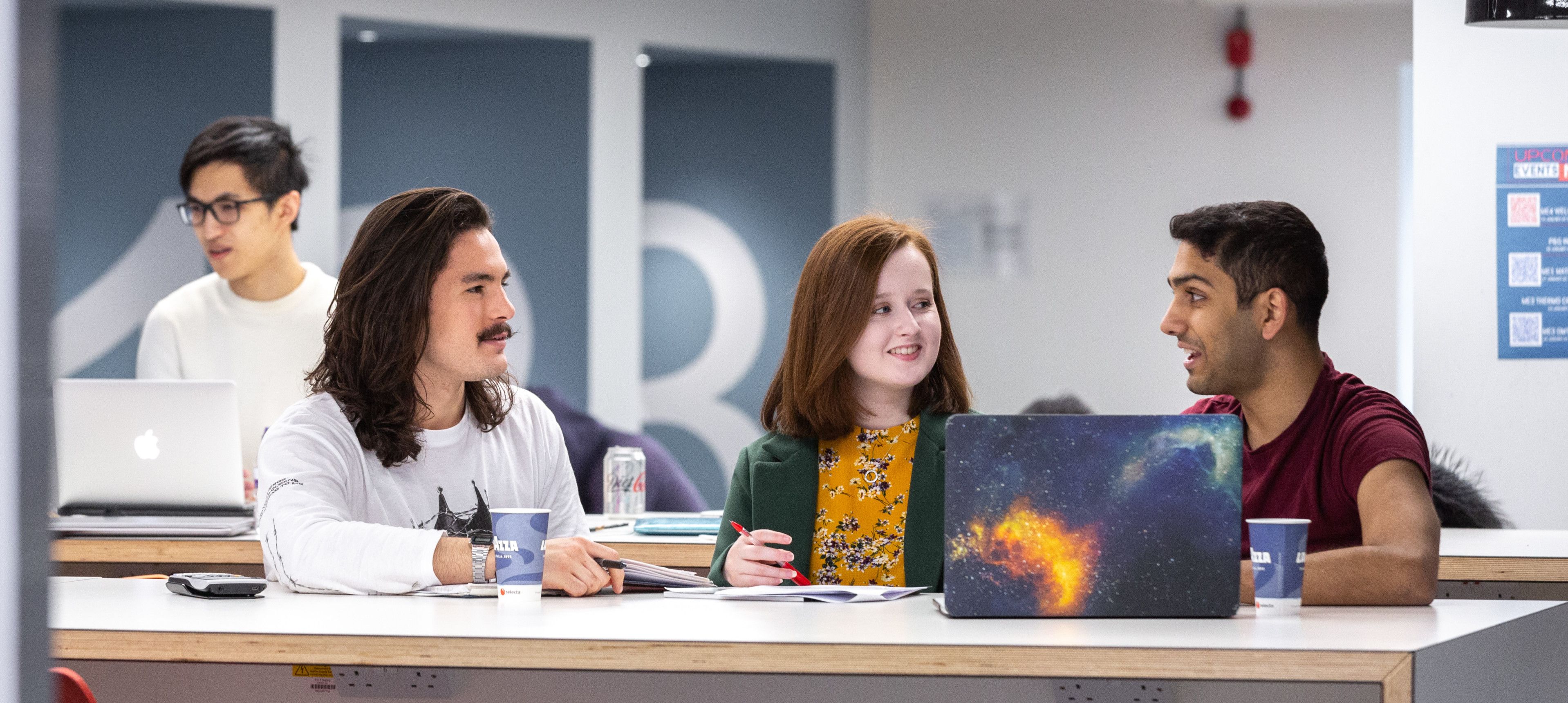 Three Imperial students sitting at a workbench with a laptop having a discussion