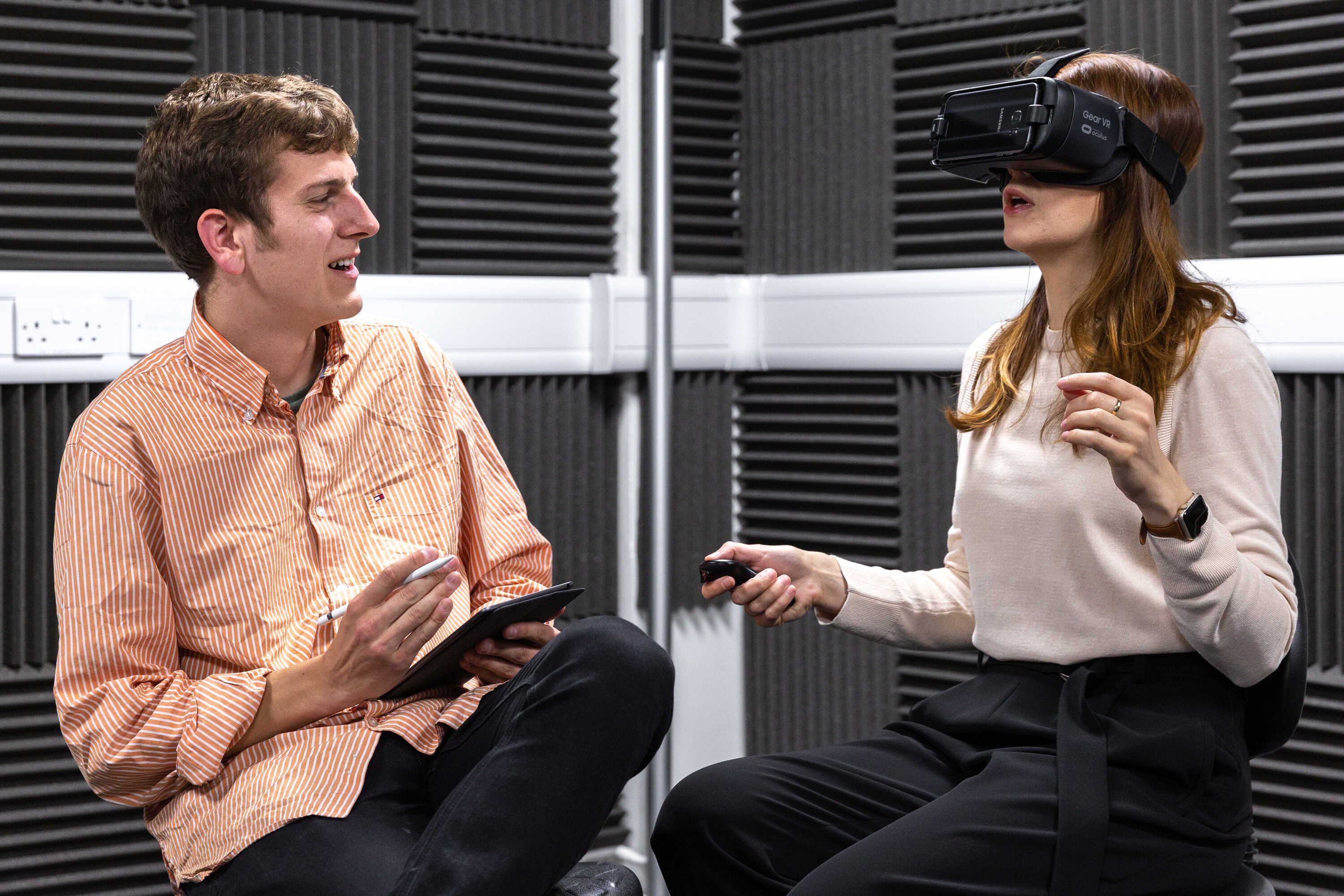 A male and female student sitting next to each other, the female student is wearing a virtual reality headset