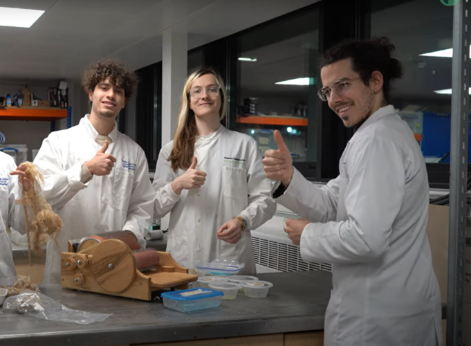 three students wearing white lab coats smiling at the camera