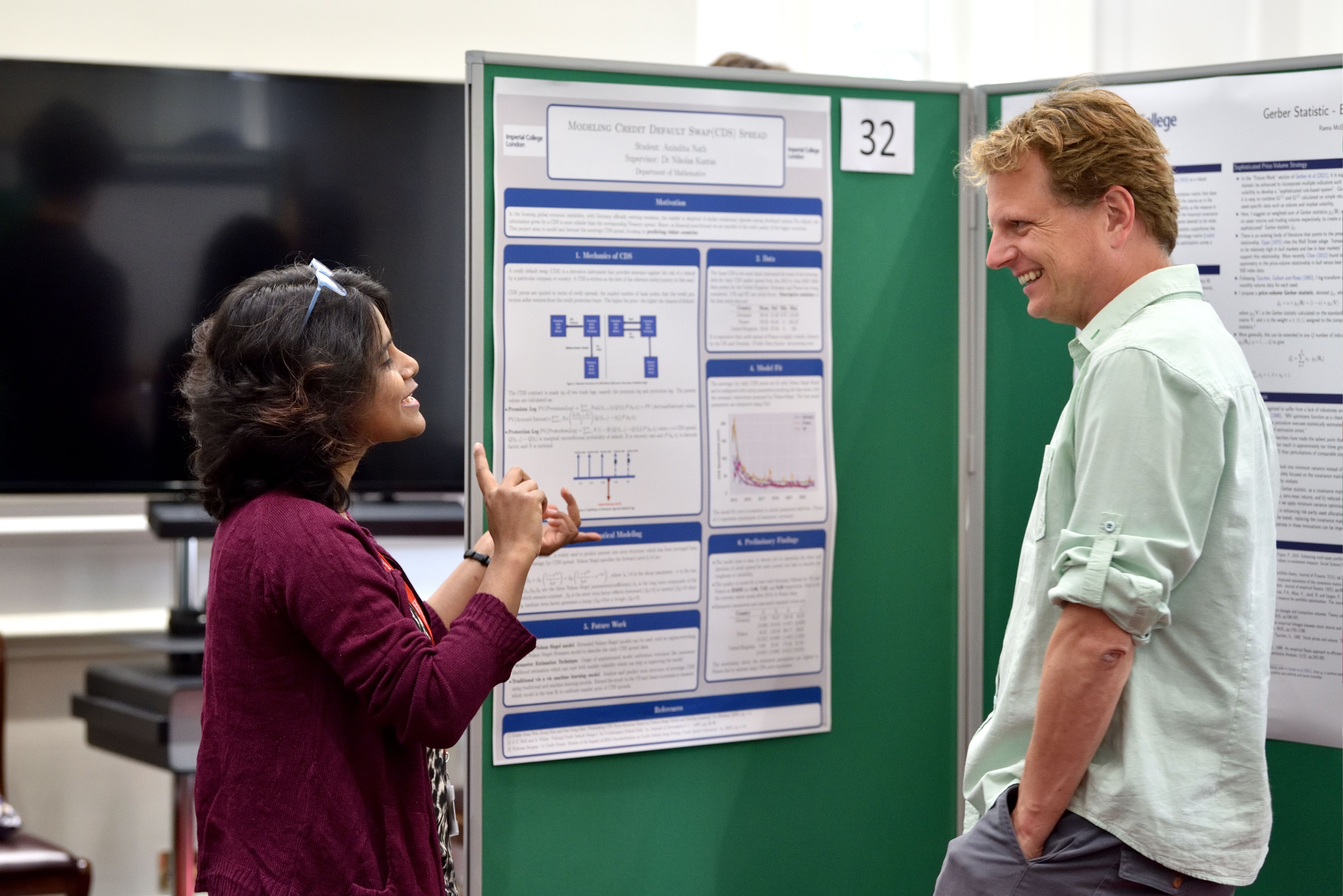 A woman and a man talking and smiling in front of panels with some graphs