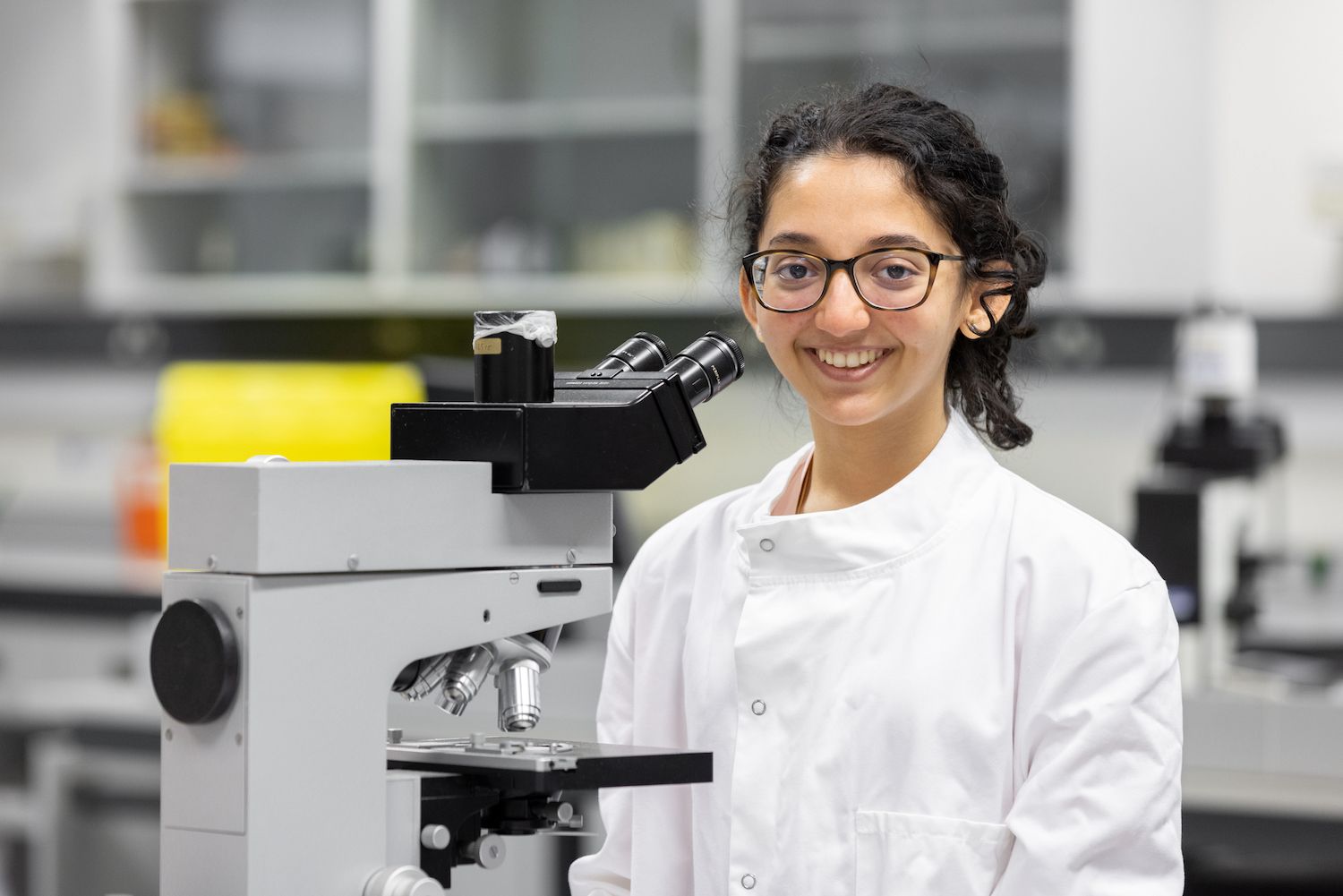 Student standing by microscope smiling