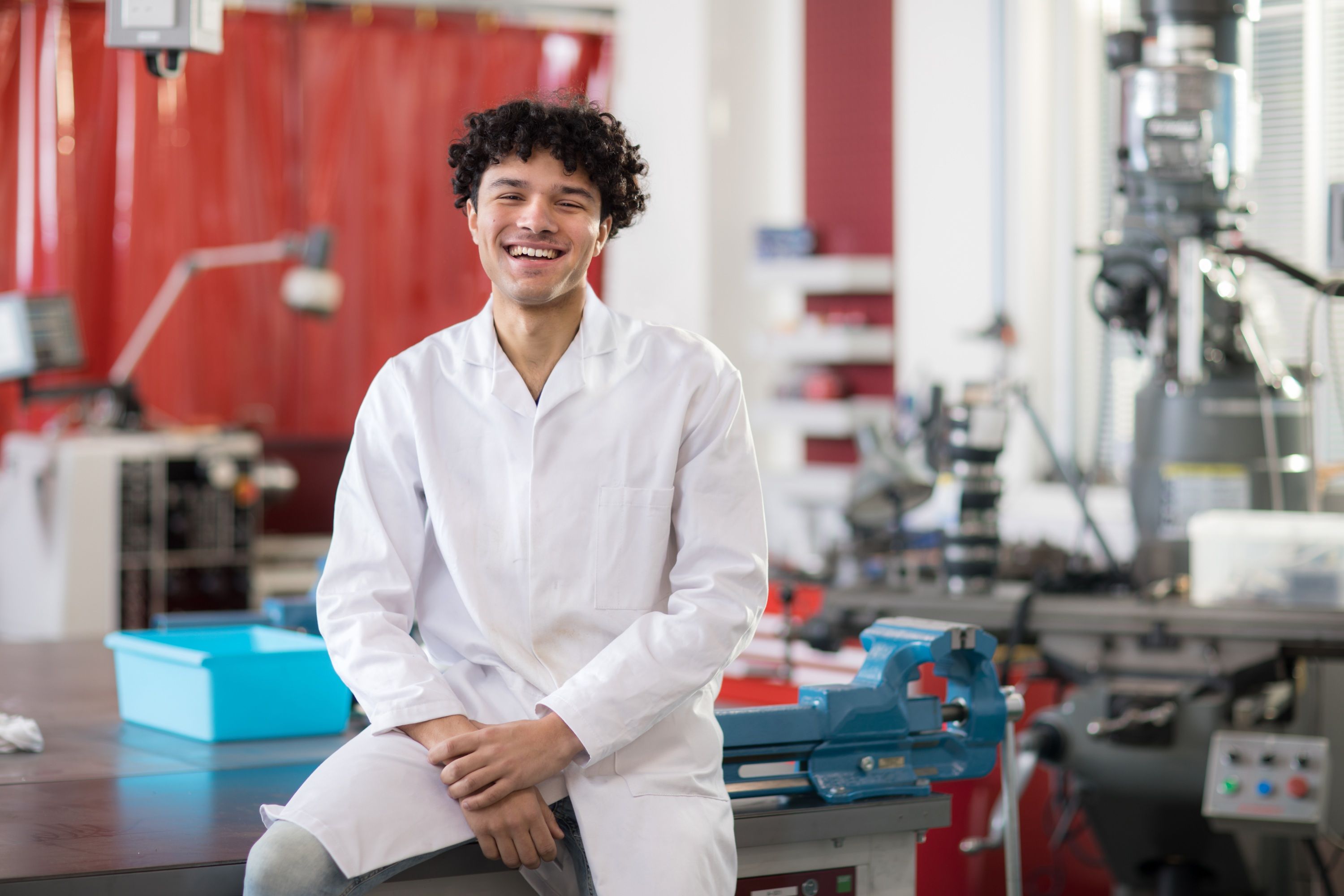 A student in a lab coat smiling at the camera