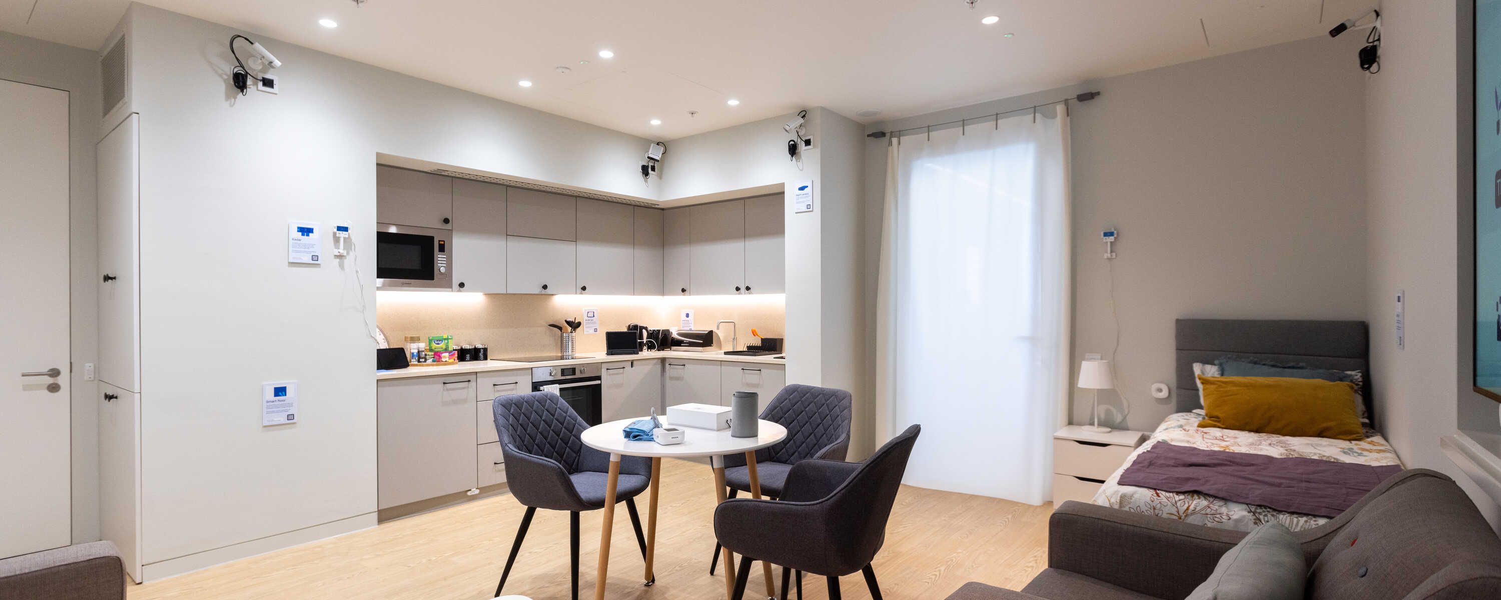 A shot of the interior of a room with a kitchen, dining table and bed. It is fitted out with cameras and sensors