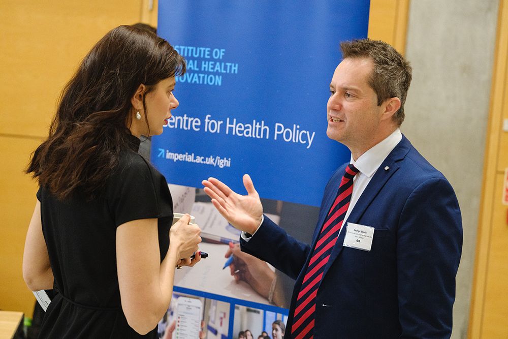 People in business attire chat in front of Centre for Health Policy banner, IGHI