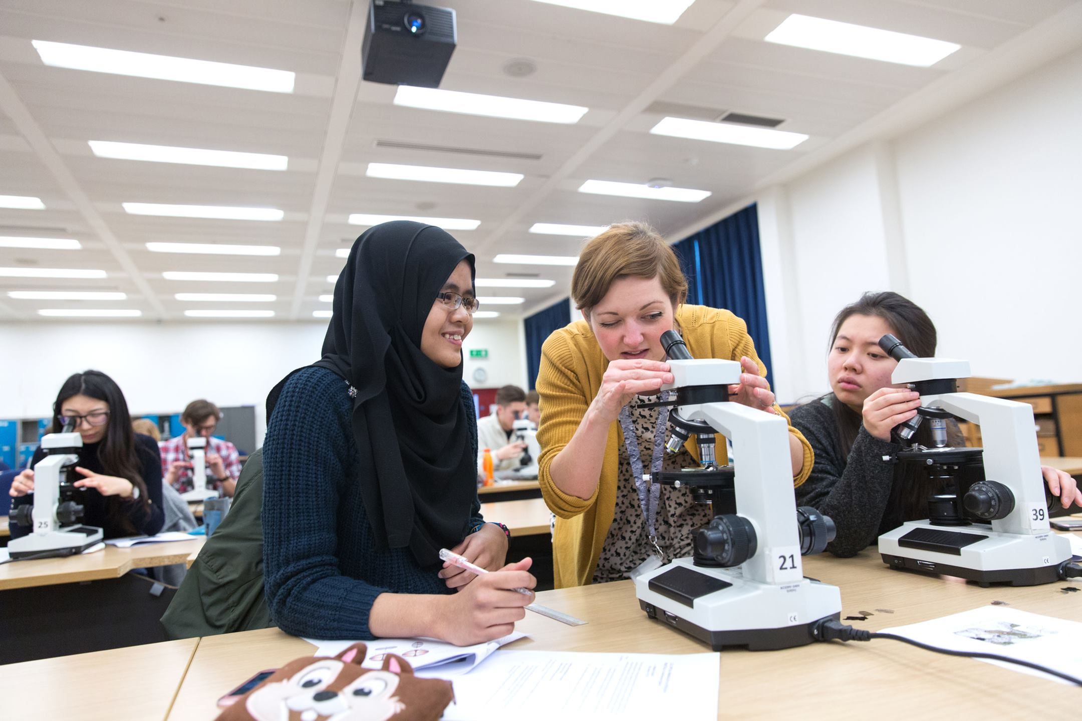 Lecturer Emma Passmore looks through a microscope with two undergraduate students during a class