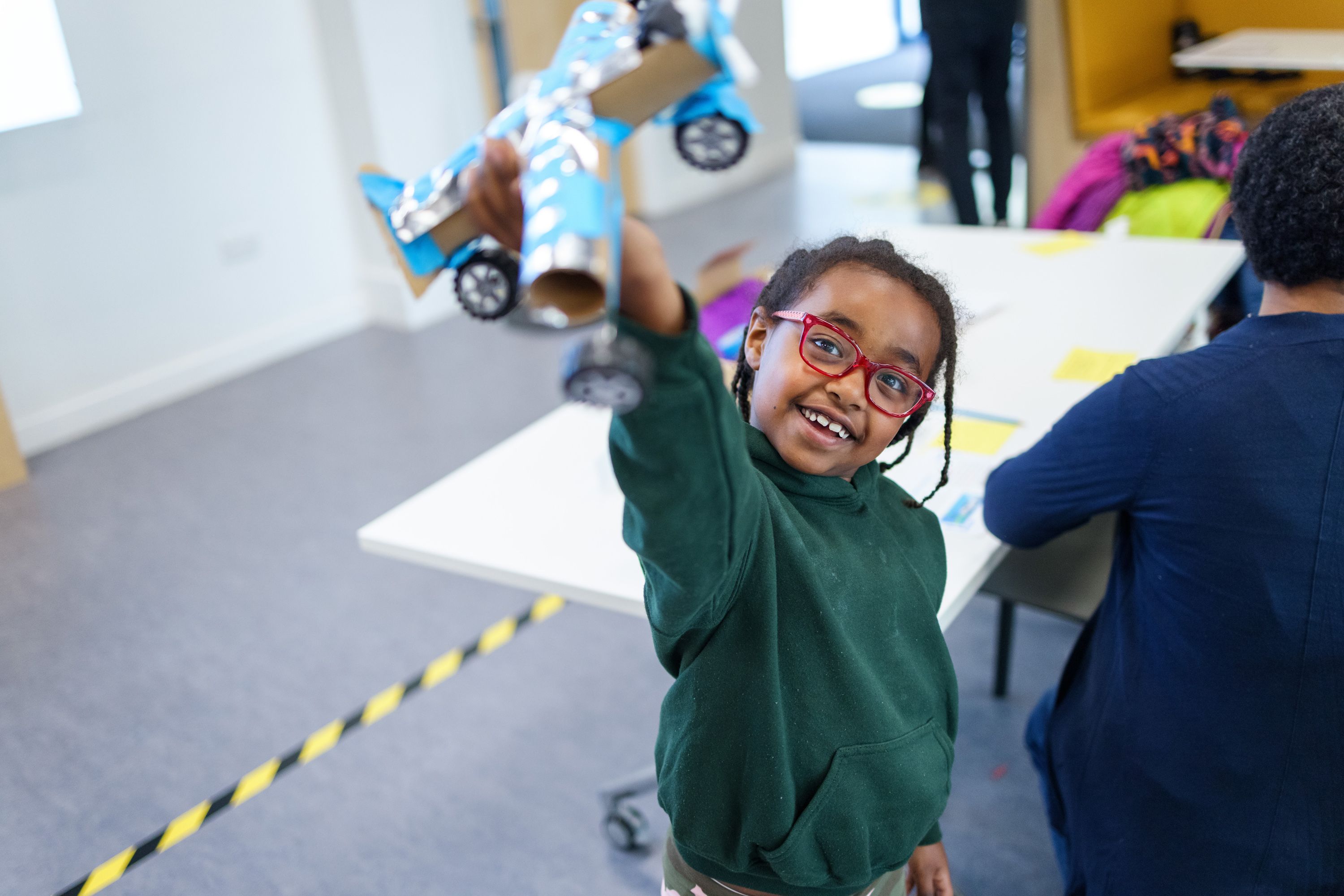 A smiling child holding a model aeroplane made out of toilet rolls