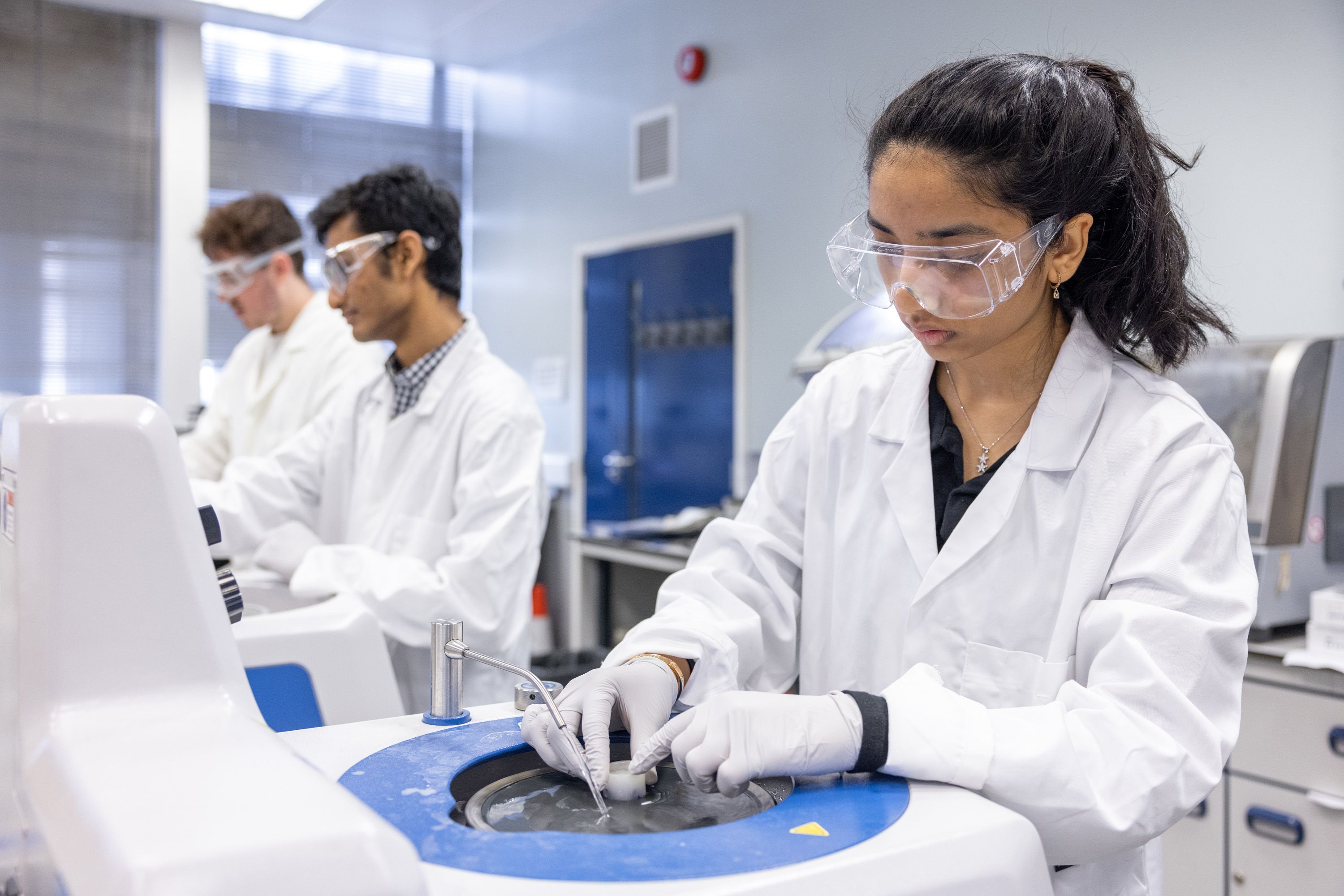 Students in lab coats using equipment in a lab