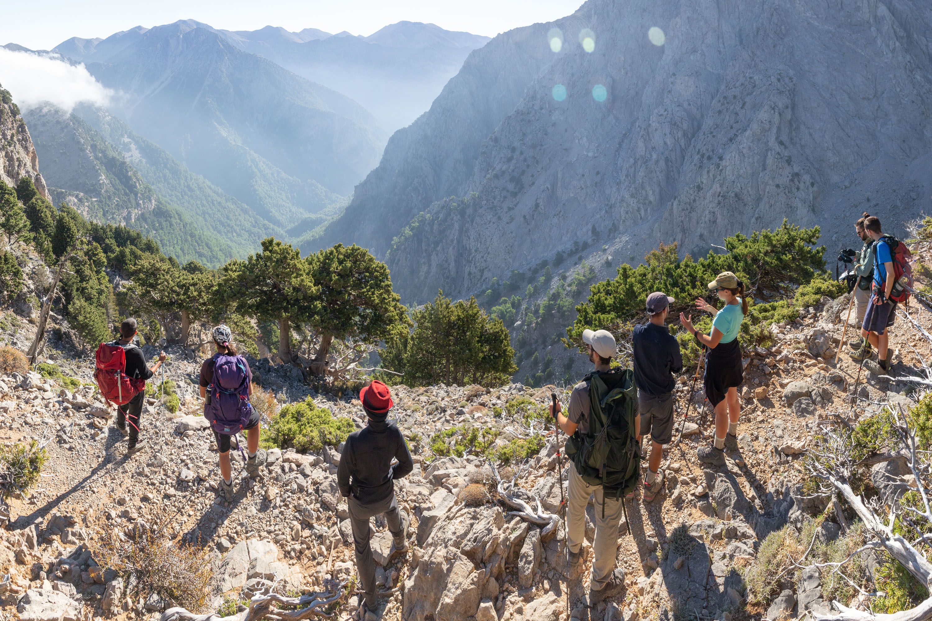 A group of students standing on a mountain in Crete in a sunny day, looking down a misty valley at mountains in the distance