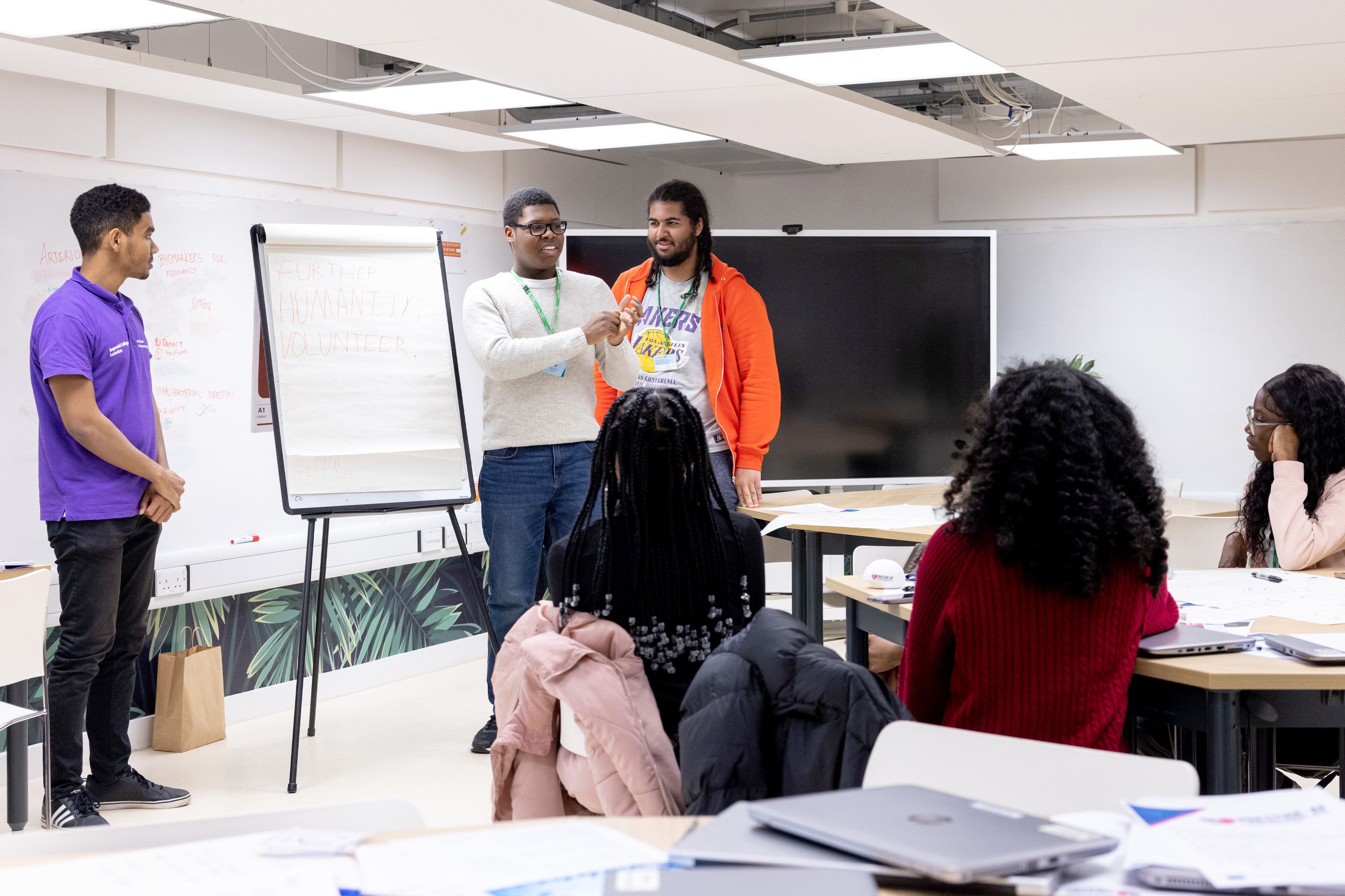 Students giving a presentation to other students, in front of a large notepad on which is written 