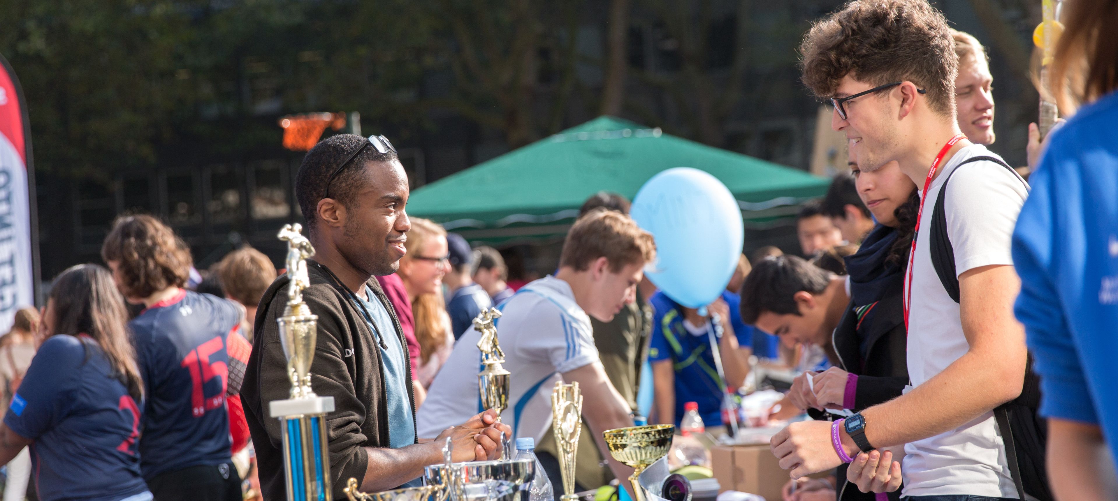 An Imperial student talking to a student behind a desk at Imperial College London Welcome Fair