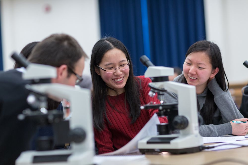 Students smiling working with microscopes and samples