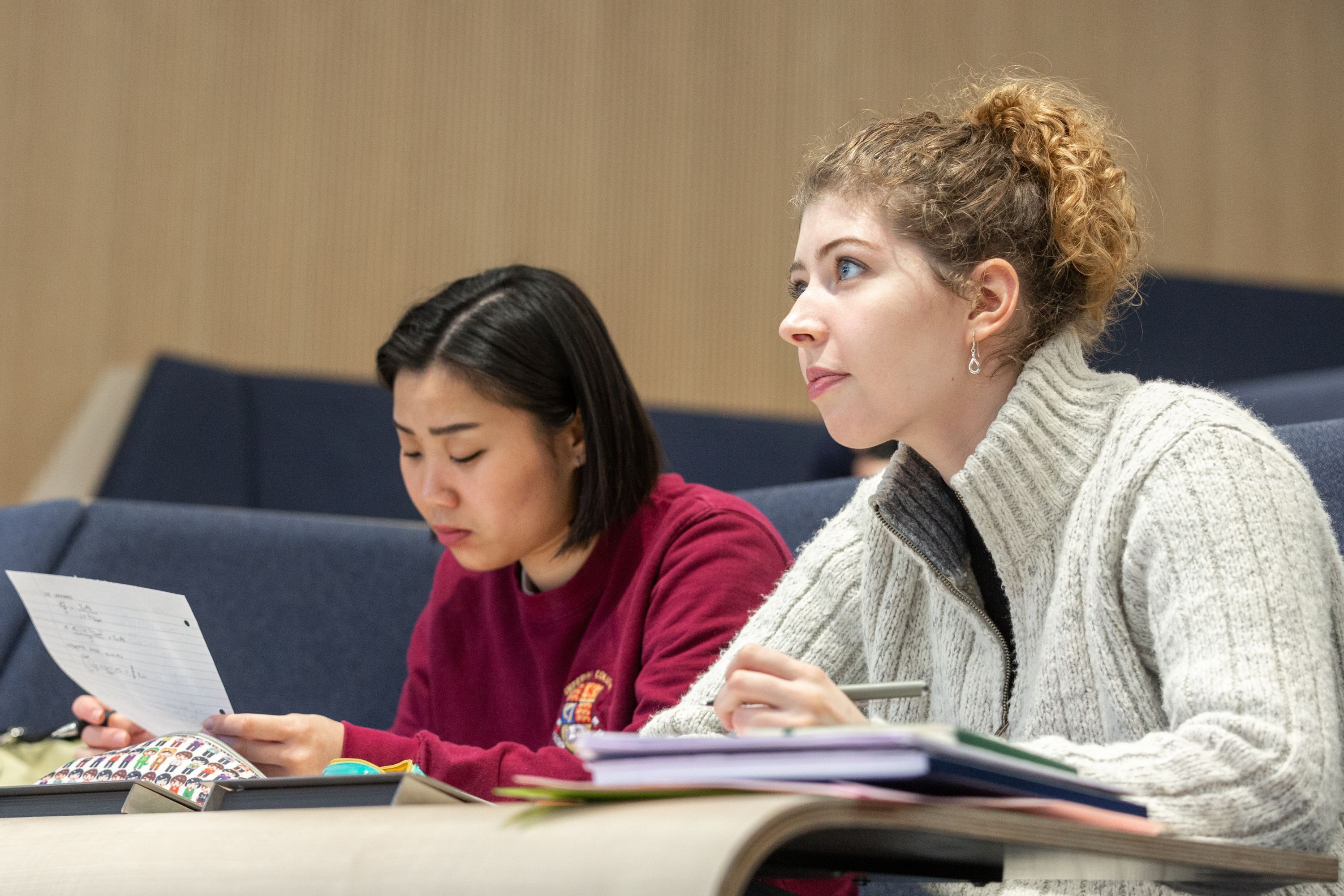 Two students in a lecture theatre writing notes