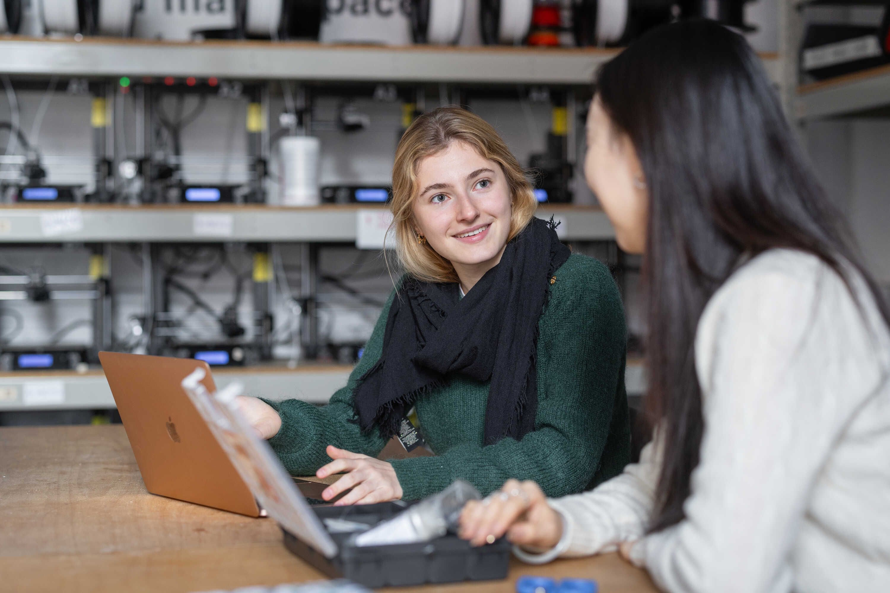 two female students sitting in front of a laptop and chatting with each other